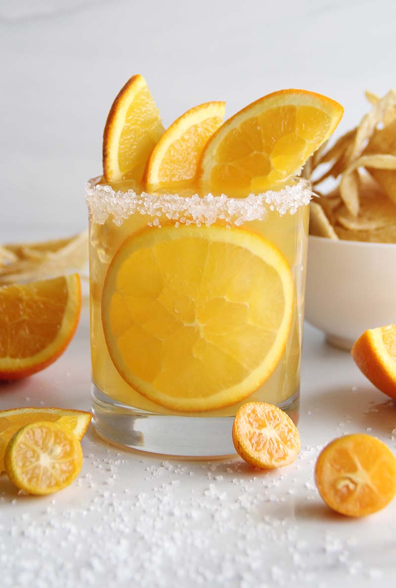 Close-up of a spiced rum margarita with orange juice and reposado tequila, served with a salted rim and paired with tortilla chips for a winter citrus cocktail party vibe.
