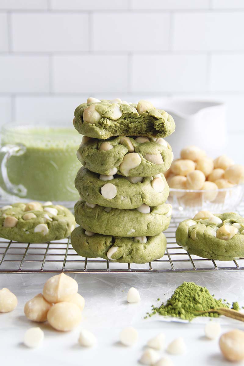 Stack of vegan gluten-free matcha white chocolate macadamia cookies with a soft, chewy interior; the top cookie in the stack has a bite taken from it.