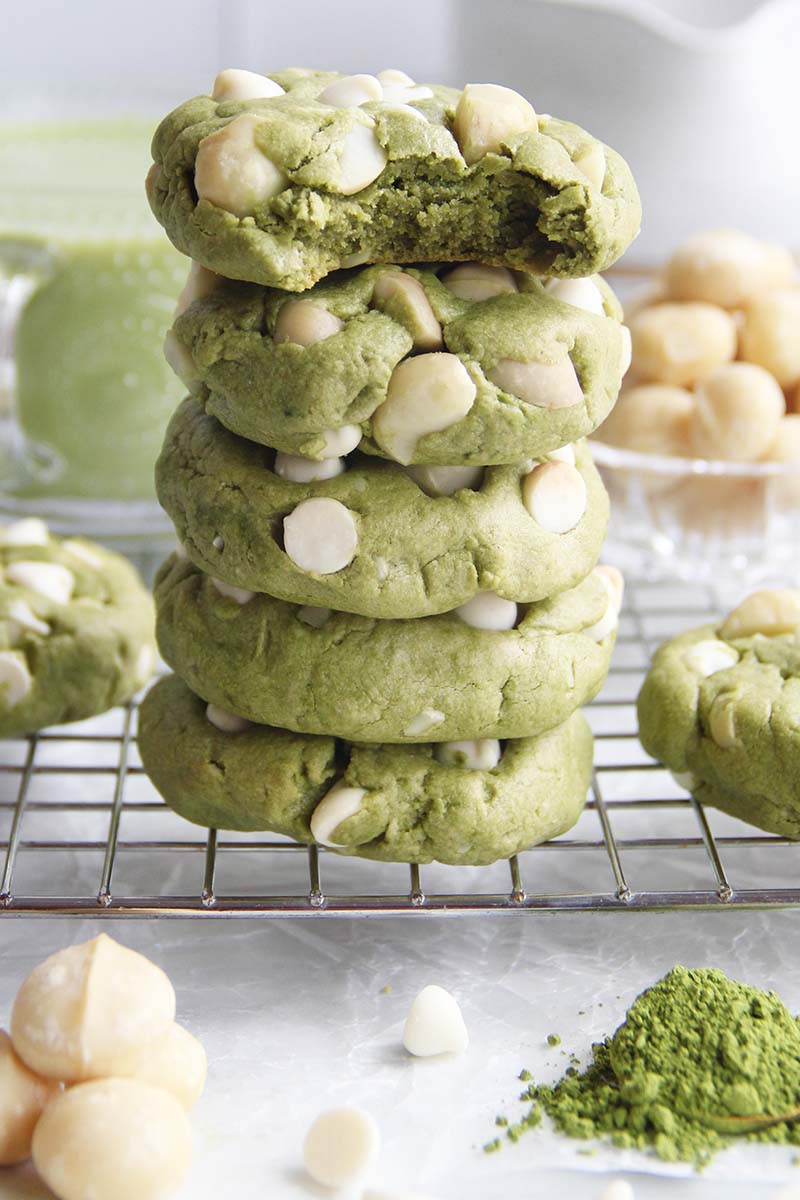 Close-up of a healthy vegan matcha cookies with white chocolate chips and macadamia nuts (one with a bite missing) showing the soft interior.