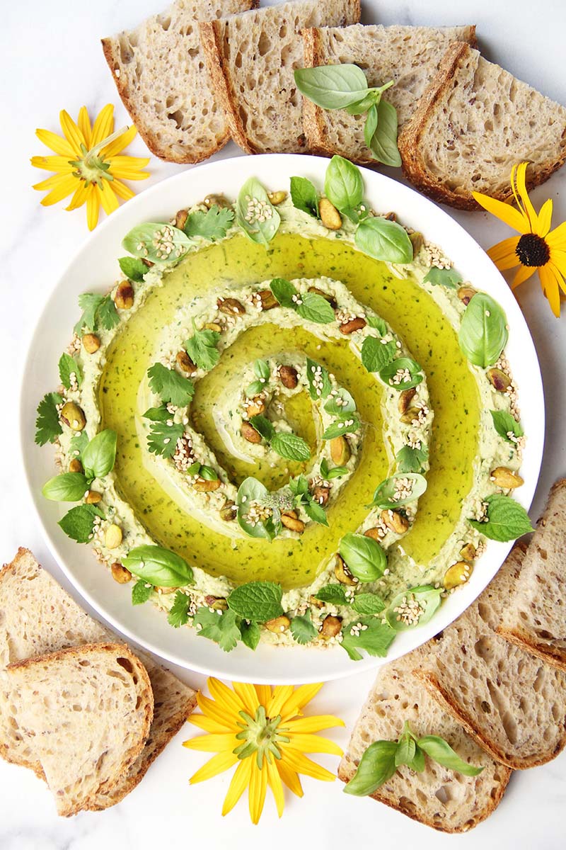 Creamy green goddess hummus served with artisan bread and topped with herbs, pistachios, and olive oil.