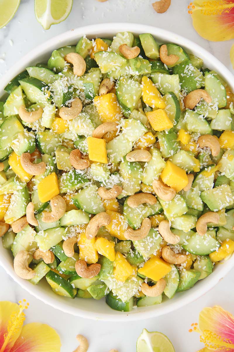 Serving bowl of Mango Cucumber Avocado Salad, garnished with cashews and coconut, drizzled with a tropical sesame lime dressing.