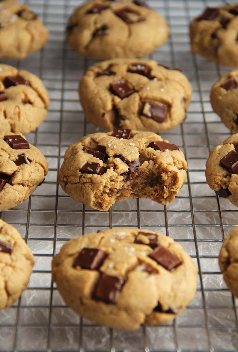 Vegan gluten-free peanut butter chocolate chunk cookies cooling on a rack; the cookie in the middle has a bite taken out of it.