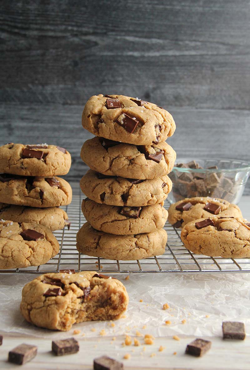 Stack of vegan gluten-free peanut butter chocolate chunk cookies on a cooling rack with scattered chocolate chunks on a wooden surface.