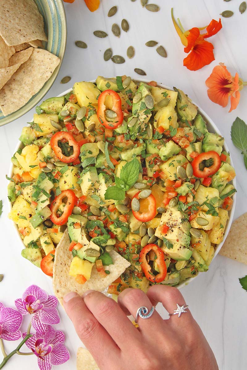 Woman's hand dipping a chip into a bowl of pineapple guacamole.