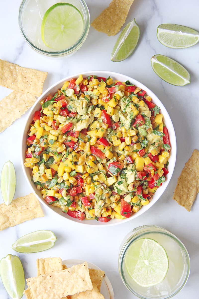 Summer corn and mango salsa served beside margaritas, shown with fresh lime wedges for a party appetizer.