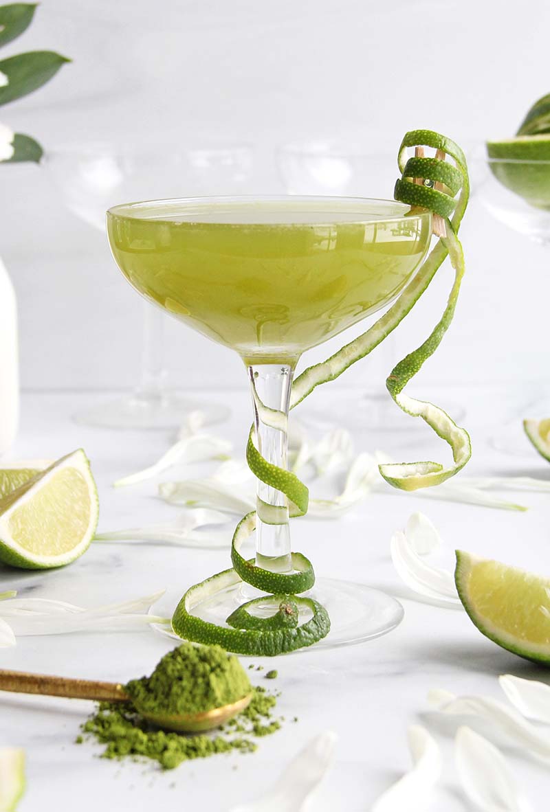 Matcha Coconut Daiquiri in a coupe glass, garnished with lime peel, and shown with bright green matcha powder in the foreground.