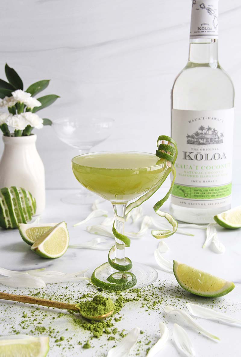 Tropical Matcha Coconut Daiquiri next to a Koloa Rum coconut rum bottle, shown in a white kitchen with a spoonful of matcha powder in the foreground.