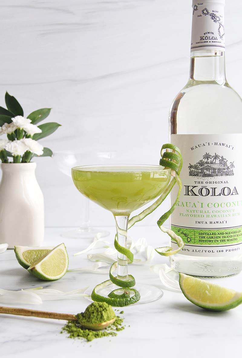 Coconut rum matcha cocktail with a lime peel garnish, shown with matcha powder and Koloa Rum coconut rum bottle.