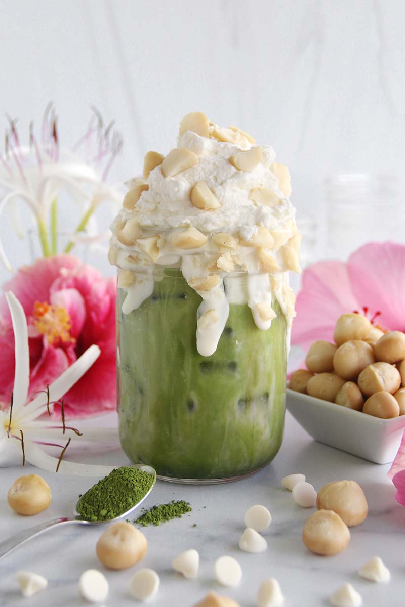 White chocolate macadamia matcha latte in a white kitchen, shown with a small dish of Hawaiian macadmia nuts.