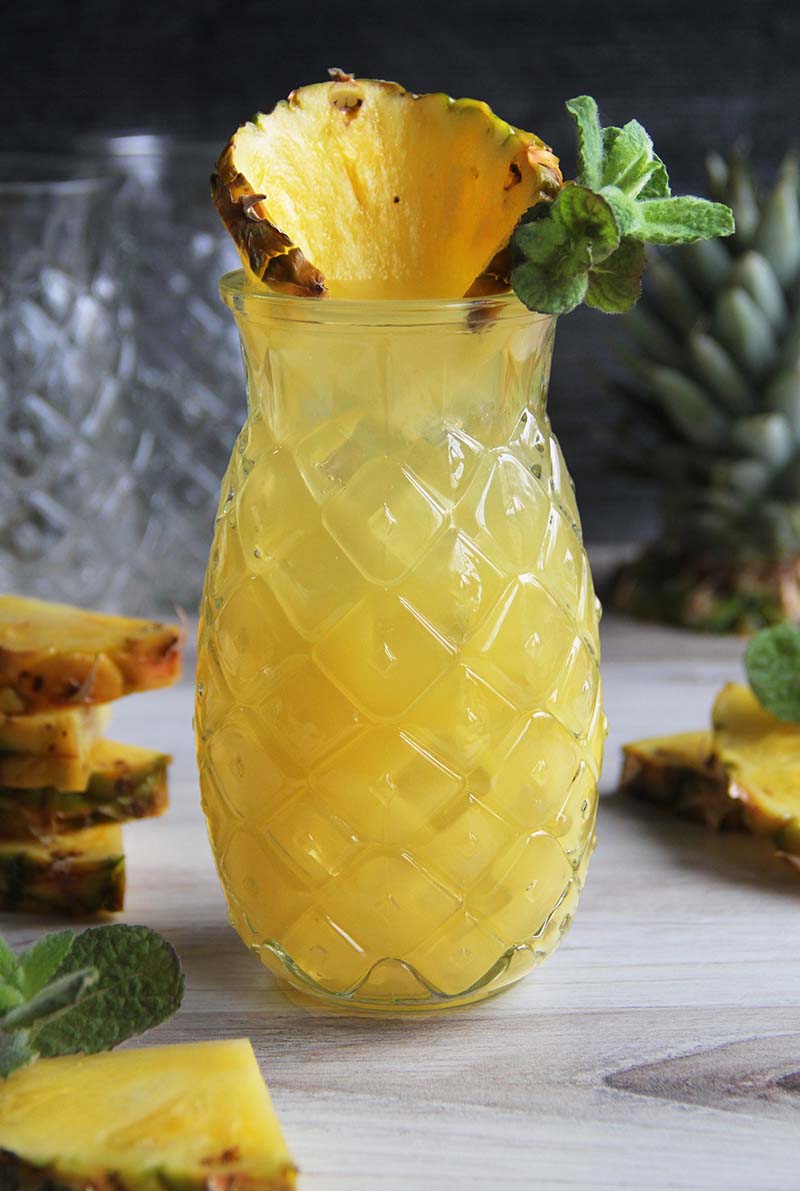 Close-up of a Pineapple Coconut Rum Fizz cocktail, shown in a pineapple-shaped glass, garnished with a pineapple slice and fresh mint.