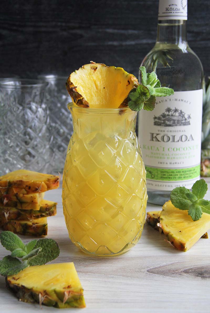 Easy Pineapple Coconut Rum Fizz cocktail, shown with a bottle of Koloa Coconut Rum and pineapple slices.