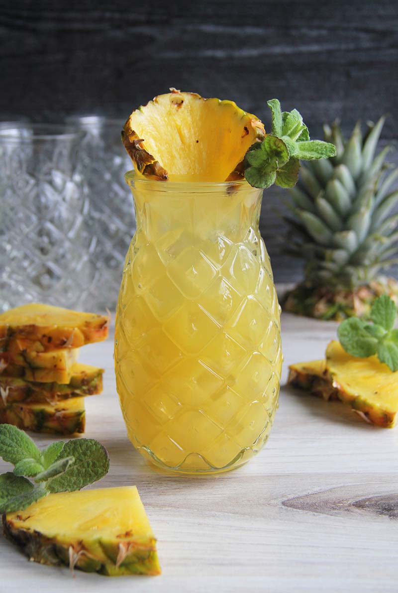 Pineapple Coconut Rum Fizz cocktail, garnished with a slice of pineapple and fresh mint, shown with pineapple wedges.