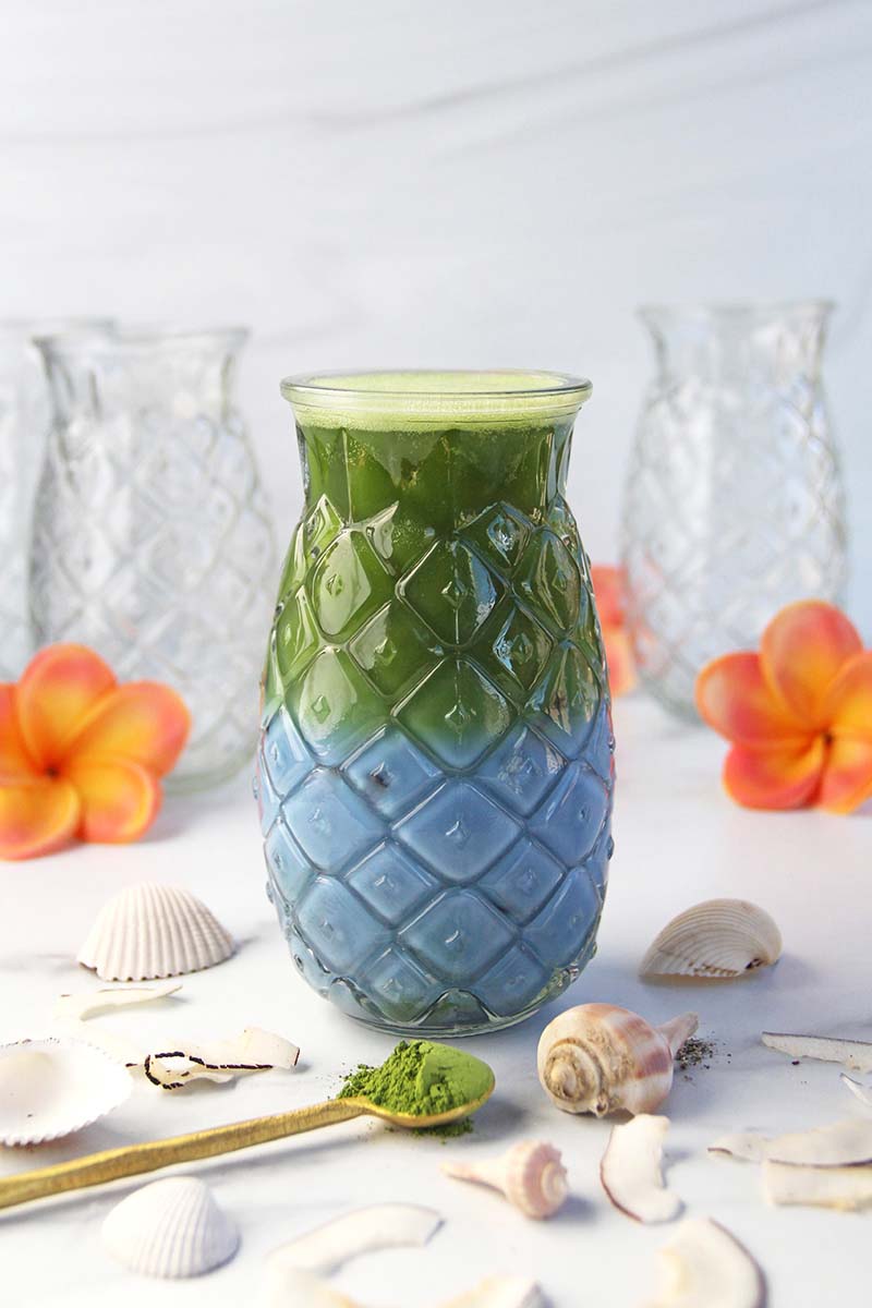 A blue matcha latte, shown in a white kitchen with orange tropical flowers.
