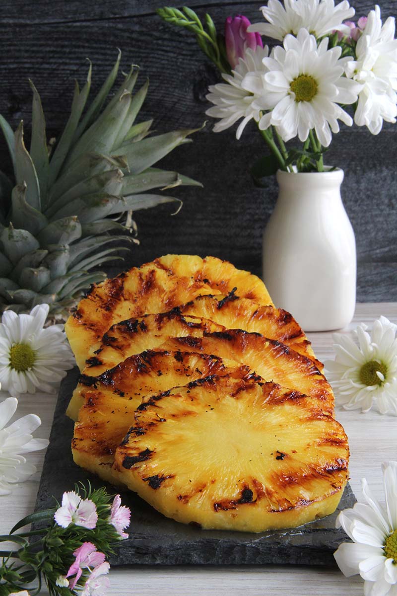 Brown Sugar Spice Rum Grilled Pineapple slices on a stone serving board, showing cross-hatched grill marks.