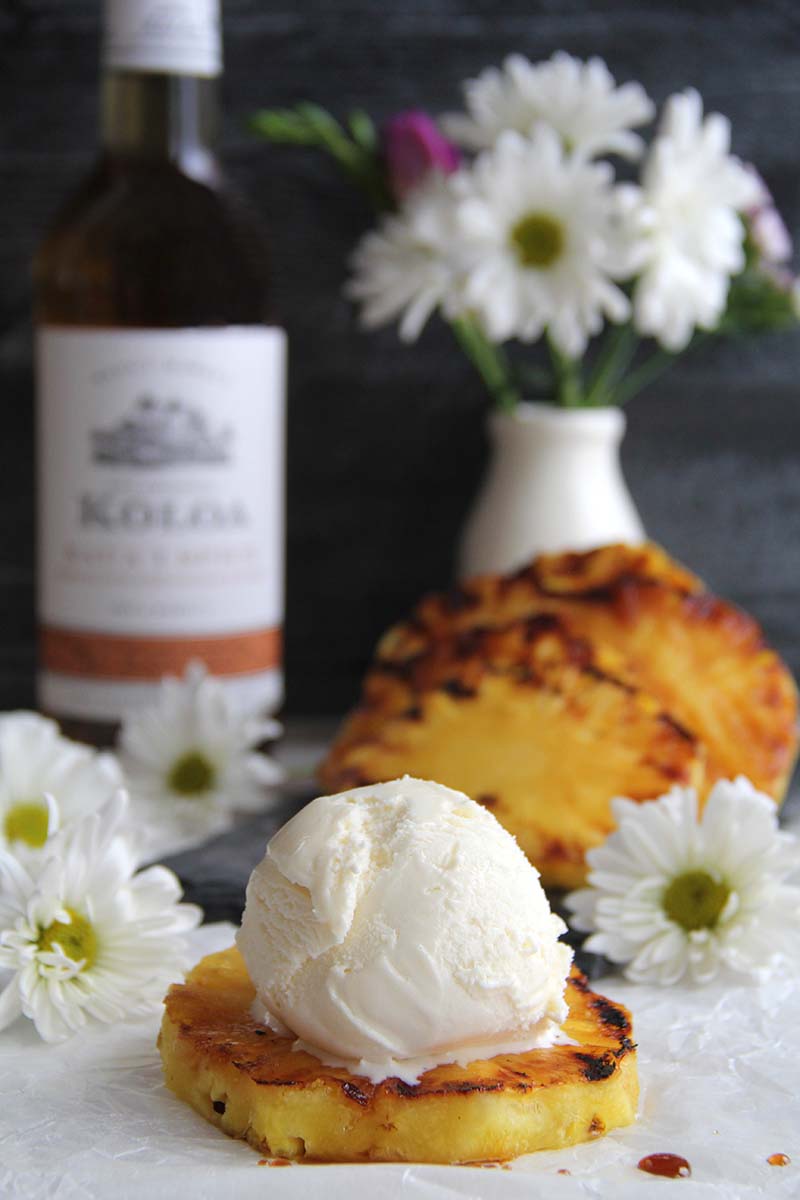 Brown Sugar Spice Rum Grilled Pineapple topped with a scoop of vanilla ice cream, shown with a bottle of Koloa Rum spiced rum in the background.