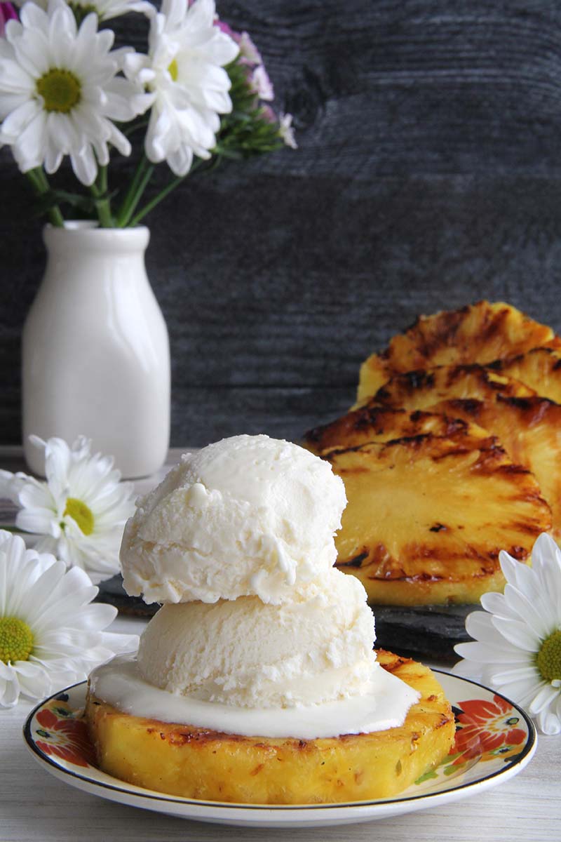 Brown Sugar Spice Rum Grilled Pineapple topped with two scoops of vanilla ice cream, shown with other grilled pineapple slices in the background.