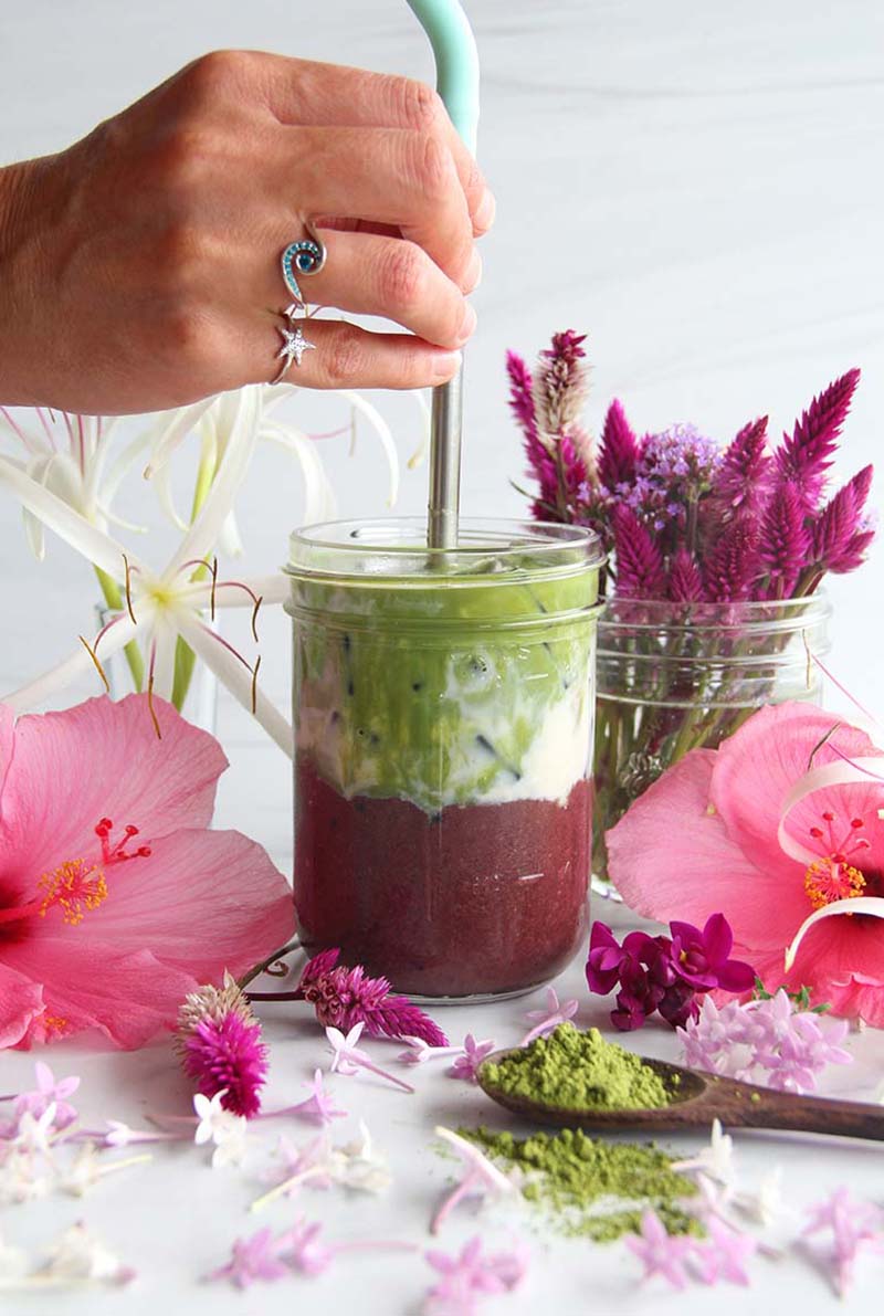 Woman's hand stirring a tropical Iced Açaí Matcha Latte with a straw.