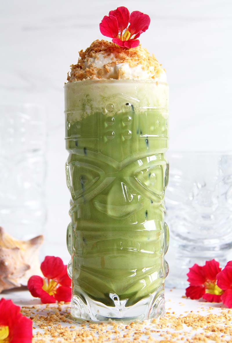 Toasted Coconut Matcha Latte, shown in a glass tiki mug, topped with coconut whip and toasted coconut.