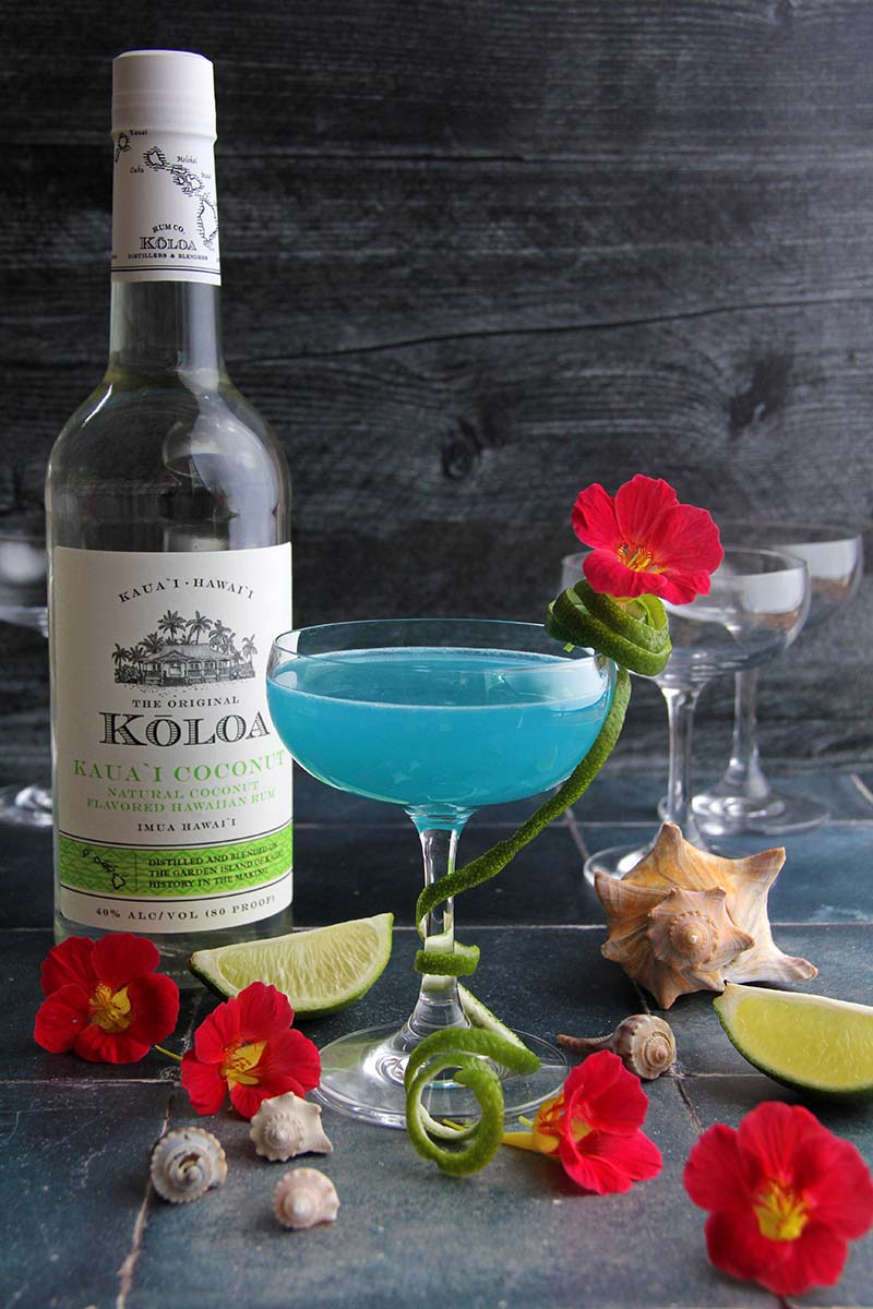 Blue Coconut Daiquiri, shown against a dark wood background next to a bottle of Koloa Rum coconut rum.