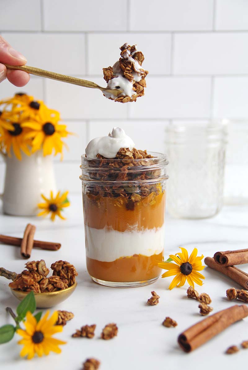 Woman's hand reaching a spoon into a pumpkin yogurt parfait.
