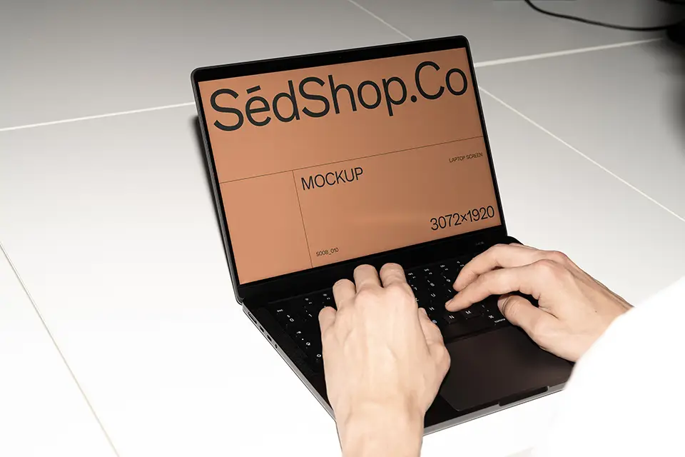 MacBook Mockup with hands typing on laptop in bright minimal workspace.