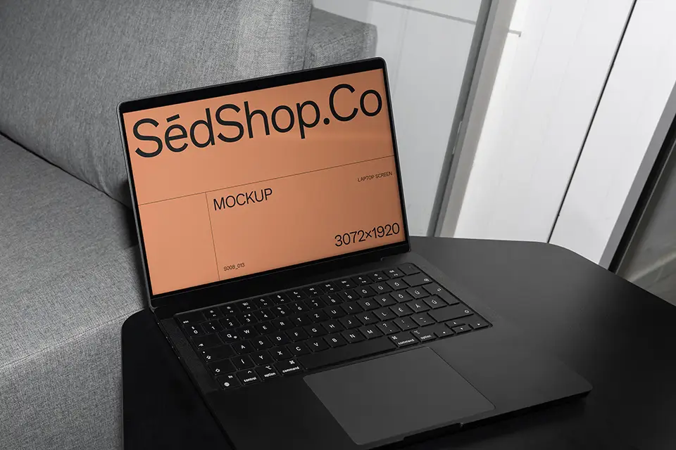 MacBook Mockup placed on black table beside grey sofa.