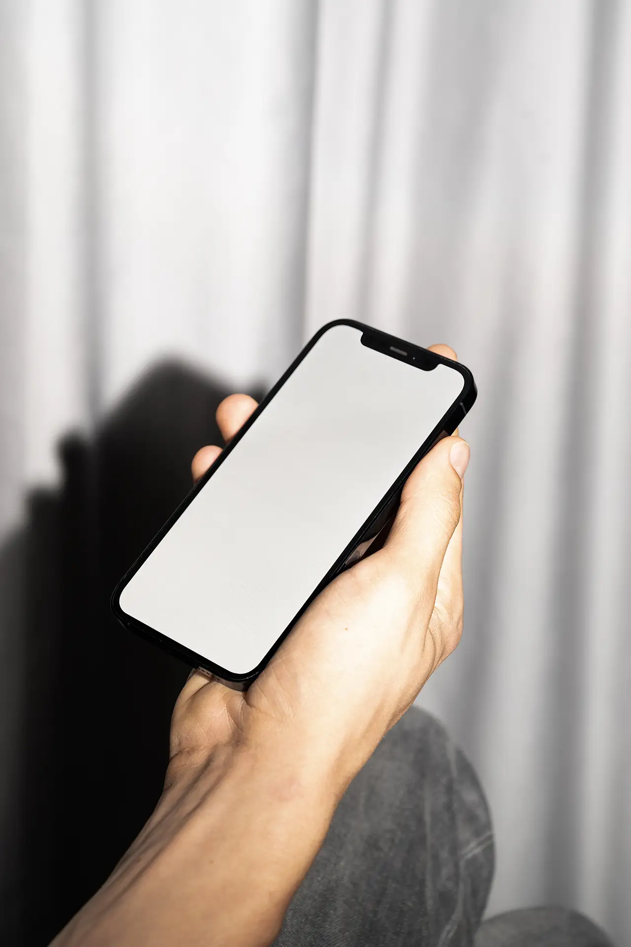 Blank iPhone Mockup in hand with flash lighting and neutral curtain background.
