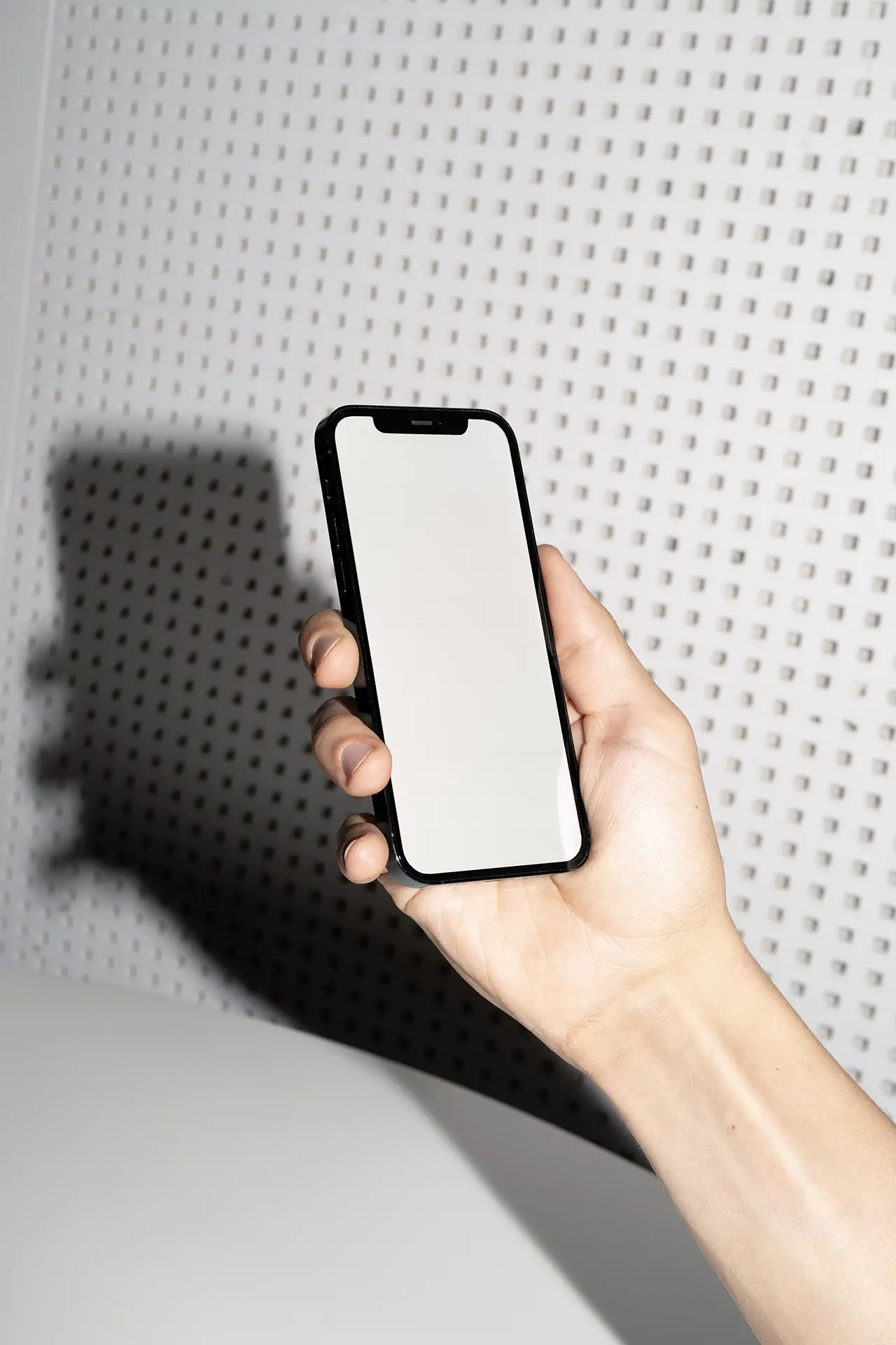 Blank iPhone Mockup photographed with flash lighting in front of a perforated wall.