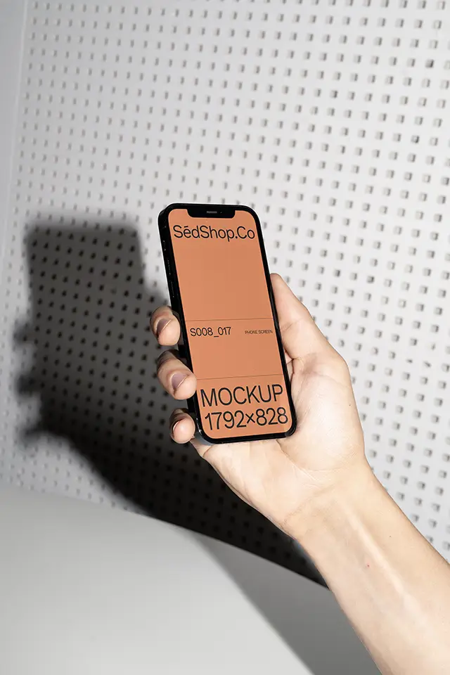 iPhone Mockup held in hand with flash lighting against perforated white wall.
