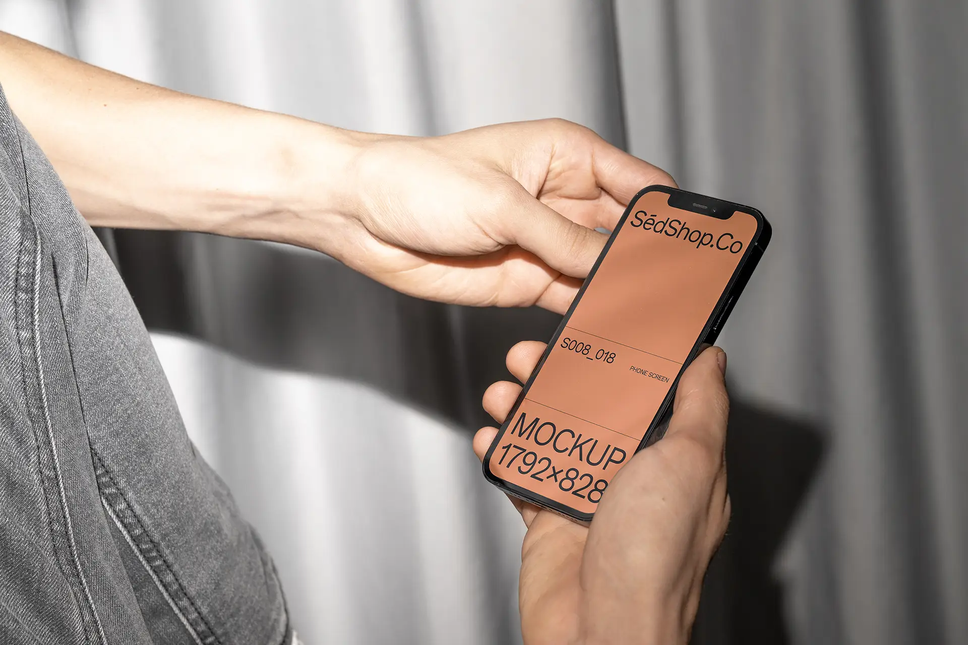 iPhone Mockup held in both hands with flash lighting and grey curtain background.