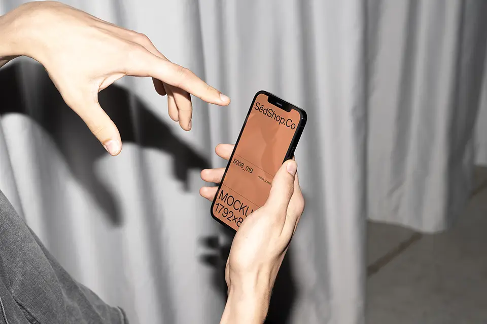 iPhone Mockup in hand with flash lighting and curtain background, finger pointing at screen.