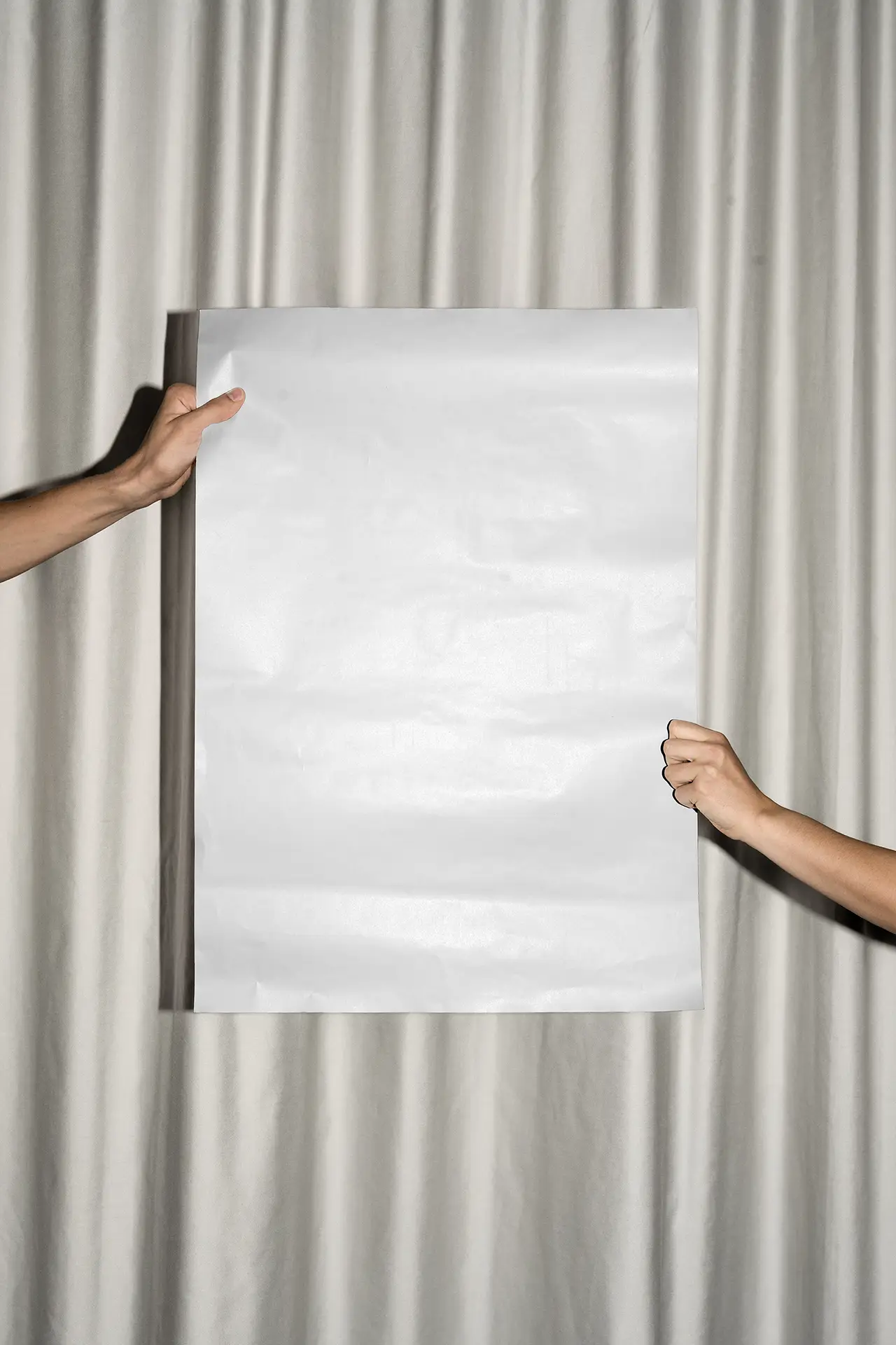 Blank poster held by two hands in front of a curtain background, illuminated with flash lighting.