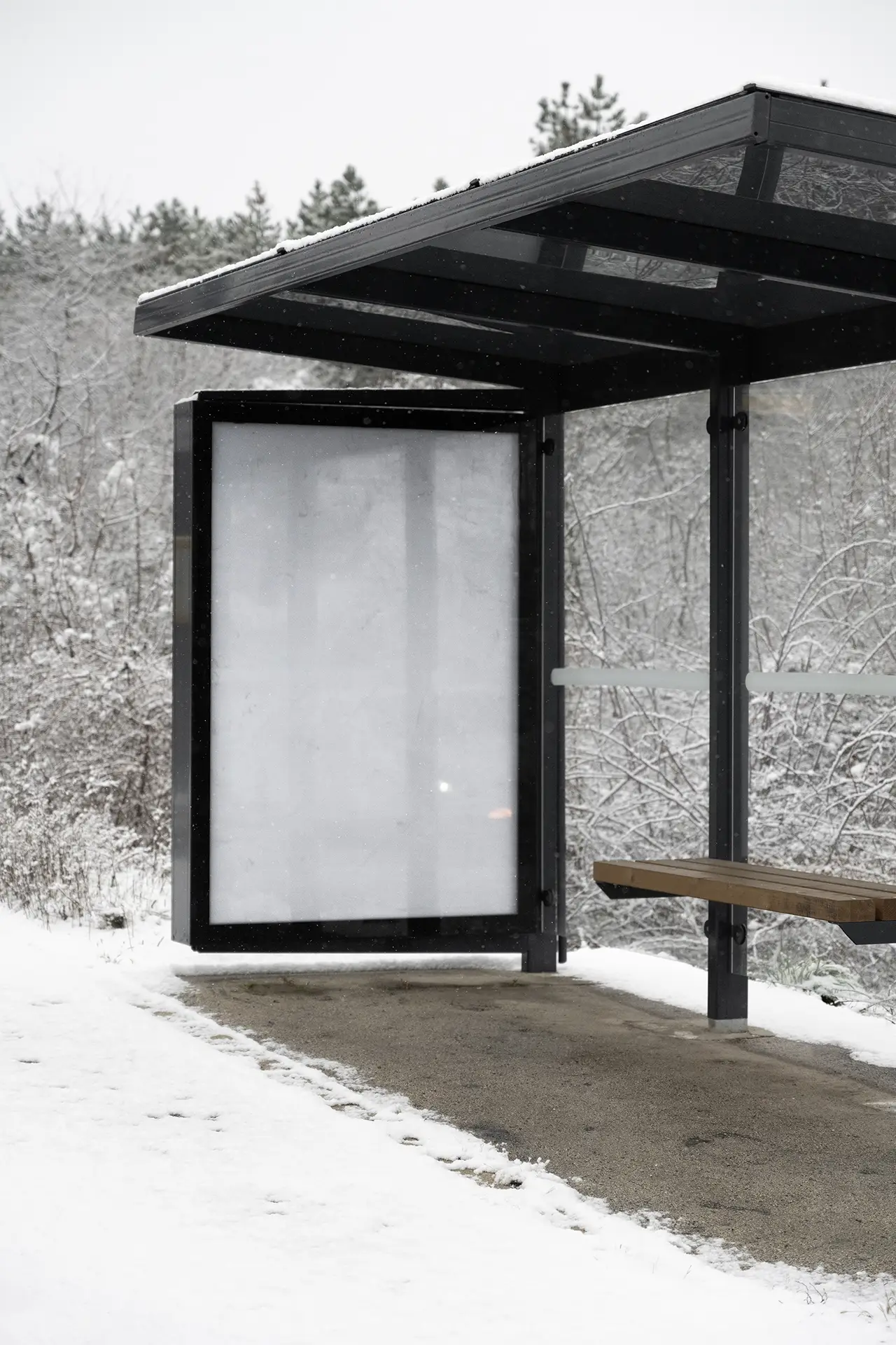 Blank vertical bus stop poster mockup in a snowy outdoor setting with frosted trees and soft diffused overcast light.