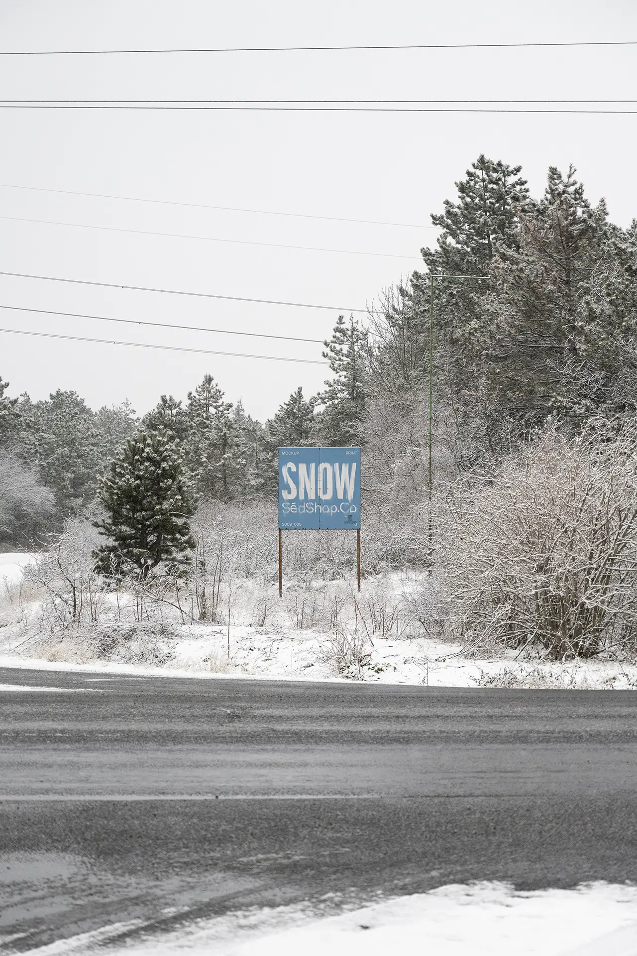 Roadside billboard mockup in a snowy forest landscape displaying a blue winter design, photographed in soft diffused overcast light.
