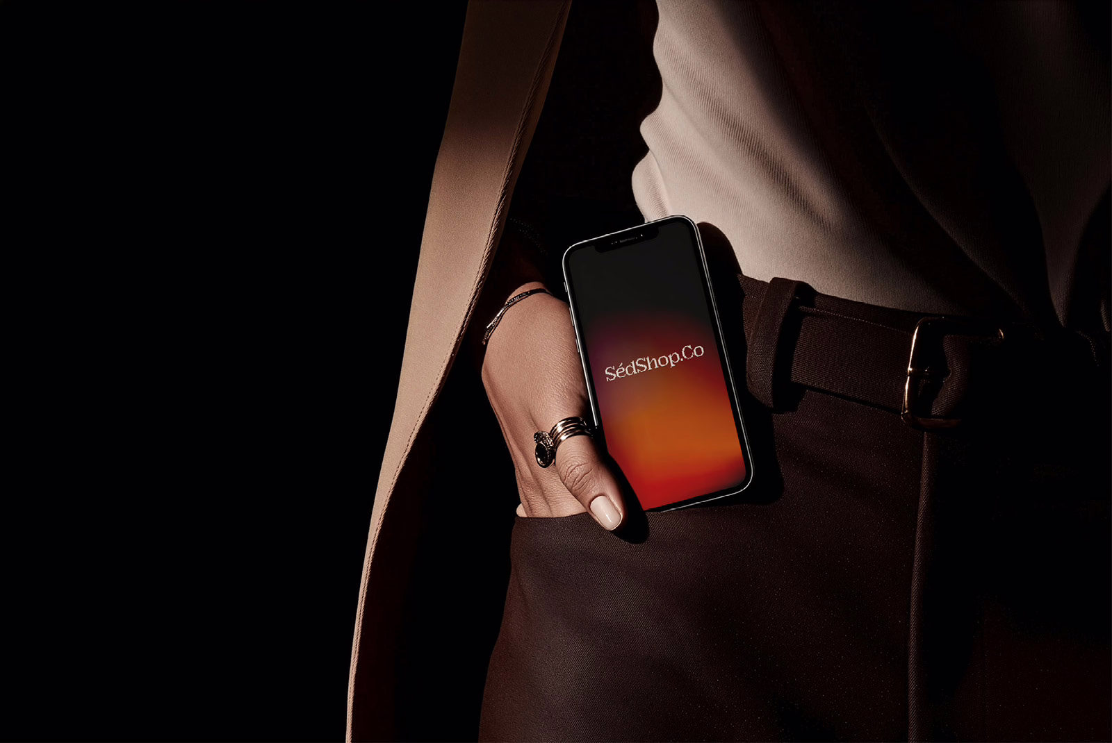 An iPhone held at the hip with a blank screen in a dark, tailored, cinematic setting.
