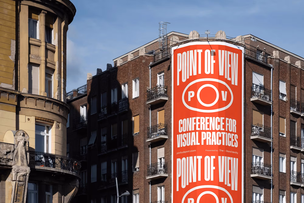 Large orange Point of View conference billboard displayed on the corner of a brick city building.
