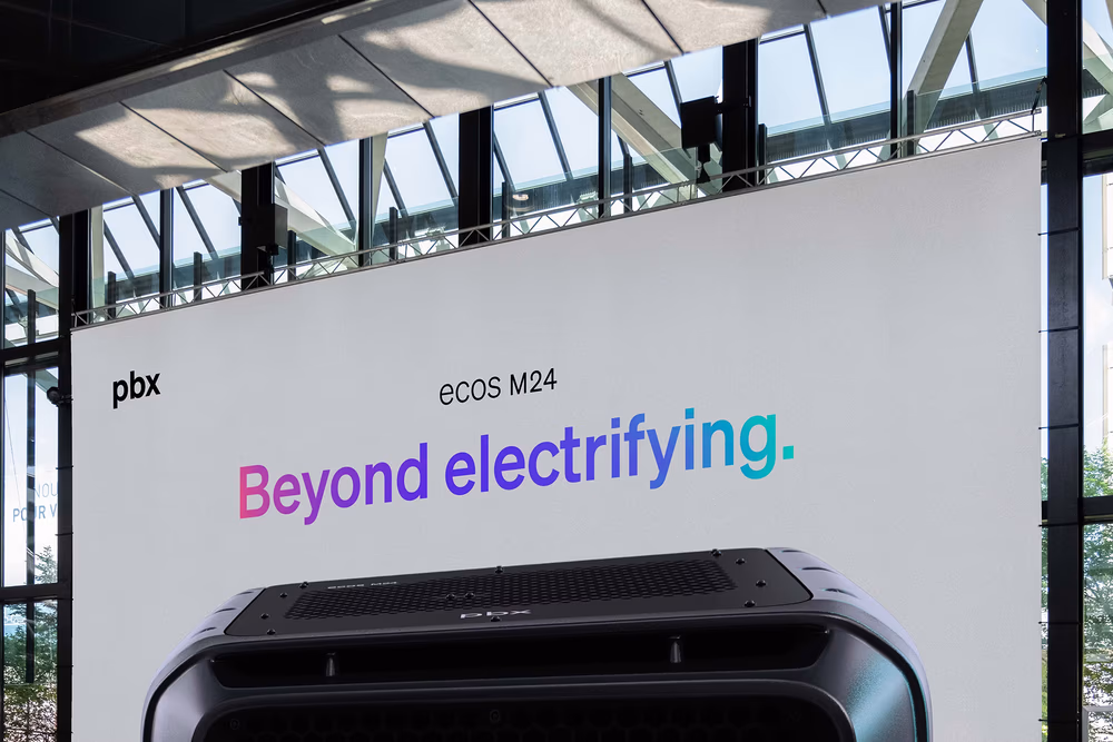 Large indoor screen displaying pbx branding and the headline “Beyond electrifying” at an exhibition venue.