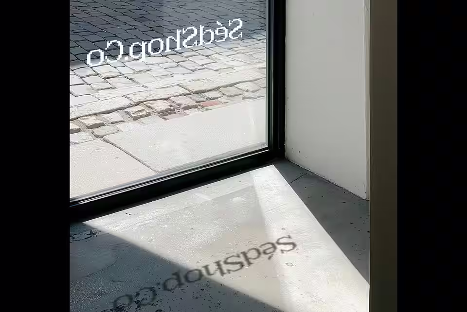 A storefront window decal with a warm gradient design casting a reflection on the floor in daylight.