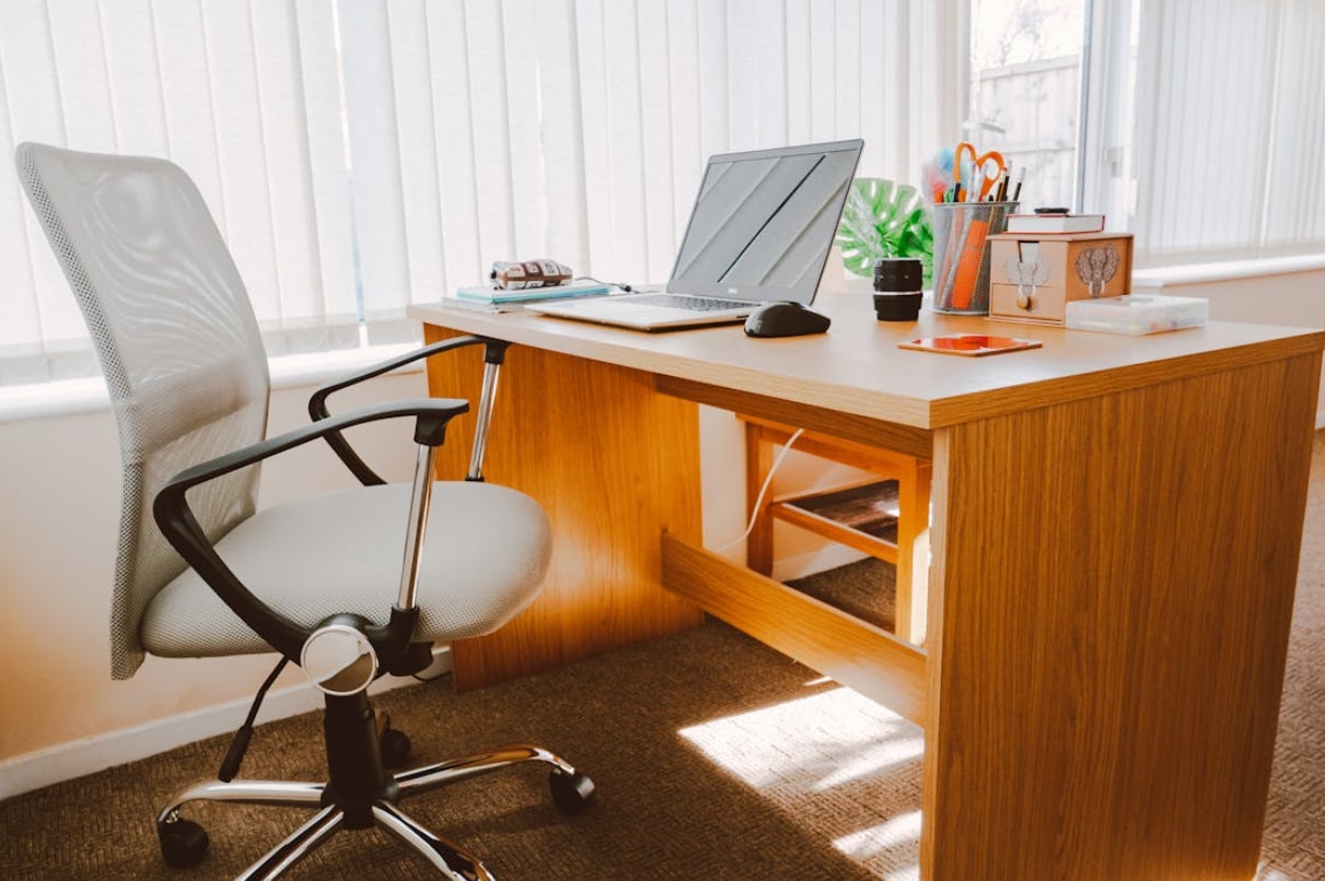 A desk with a laptop and chair positioned in front of a large window, allowing natural light to illuminate the workspace.
