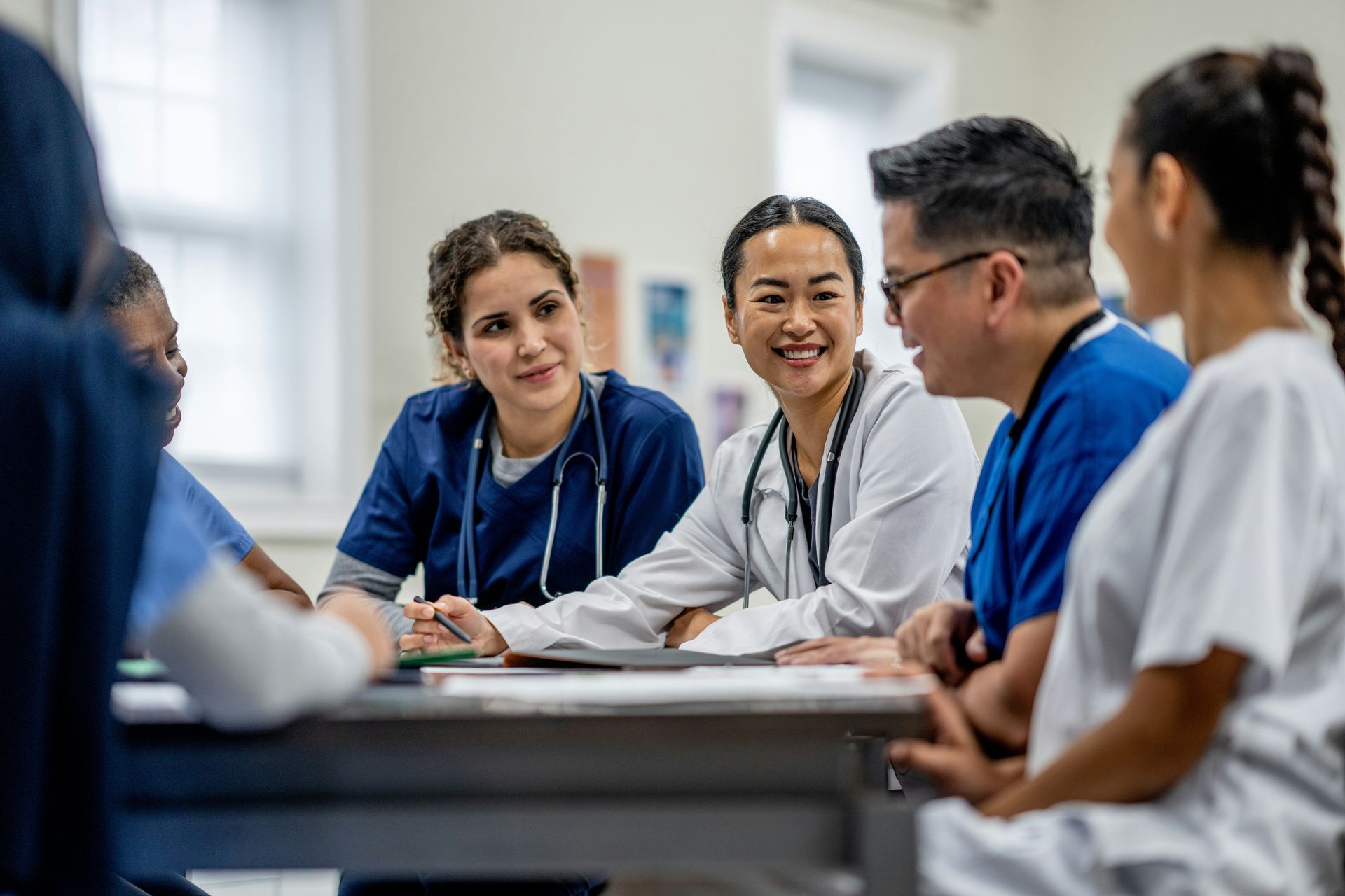 A diverse team of doctors and nurses in scrubs meeting around a table to discuss patient care