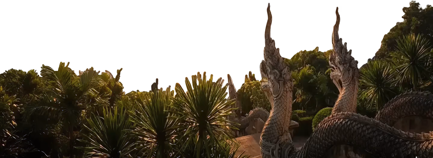Stone serpent statues surrounded by lush green tropical plants at sunset.