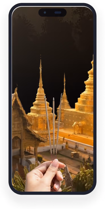 Hand holding three incense sticks with golden temple pagodas in the background at dusk.