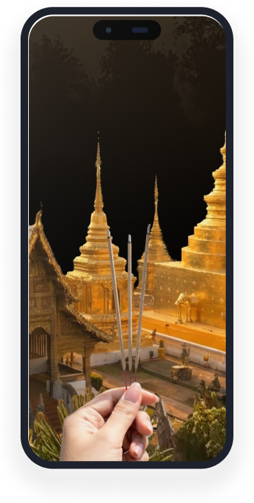 Hand holding three incense sticks with golden temple pagodas in the background at dusk.