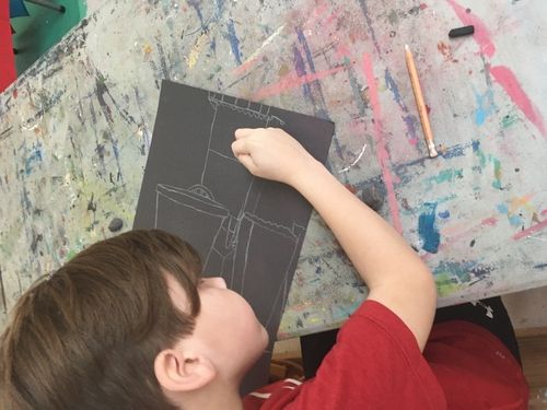 A child wearing red drawing on black paper with a white lead