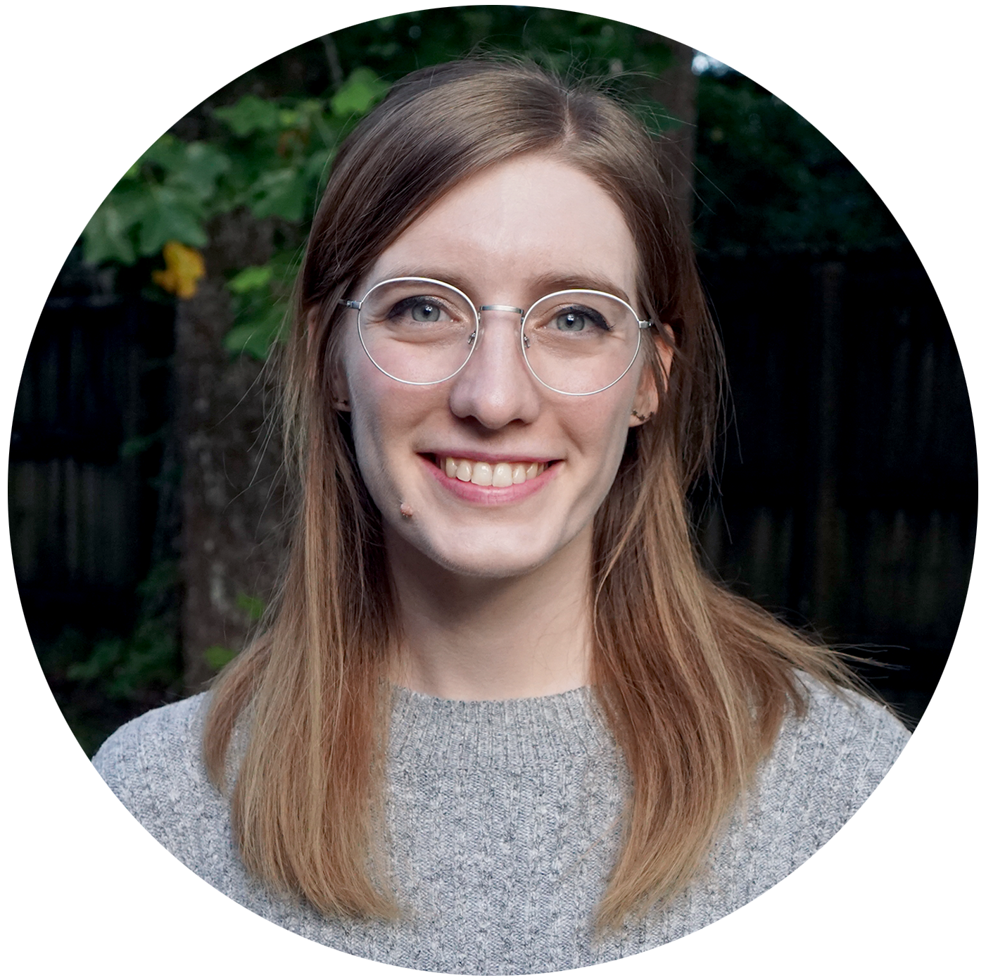 Photo of a young woman with brownish-blonde hair and glasses wearing a gray sweater.