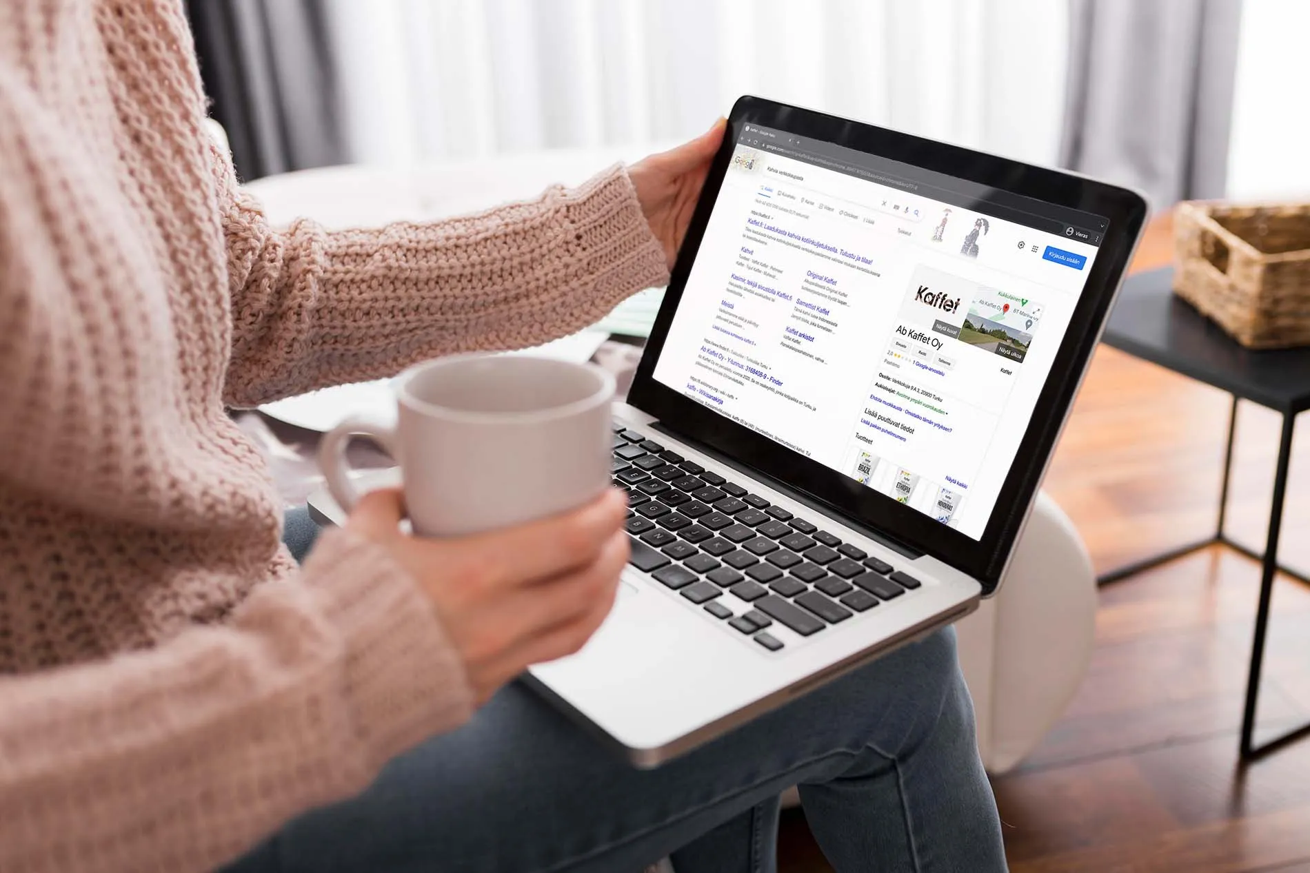 Nainen läppäri sylissään ja kahvikuppi kädessä