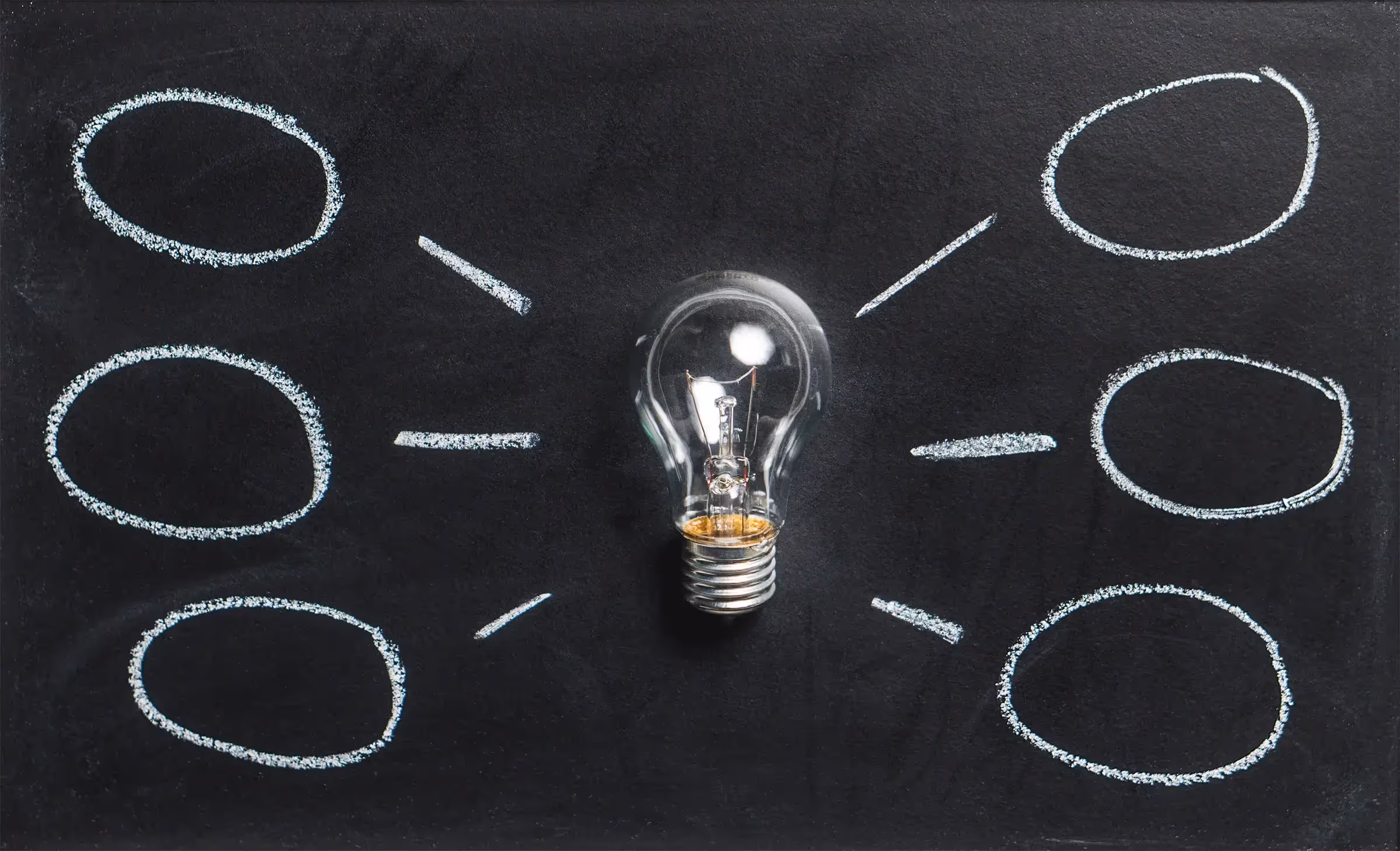 A lightbulb against a blackboard with drawn mindmap bubbles around it - UserVoice Images
