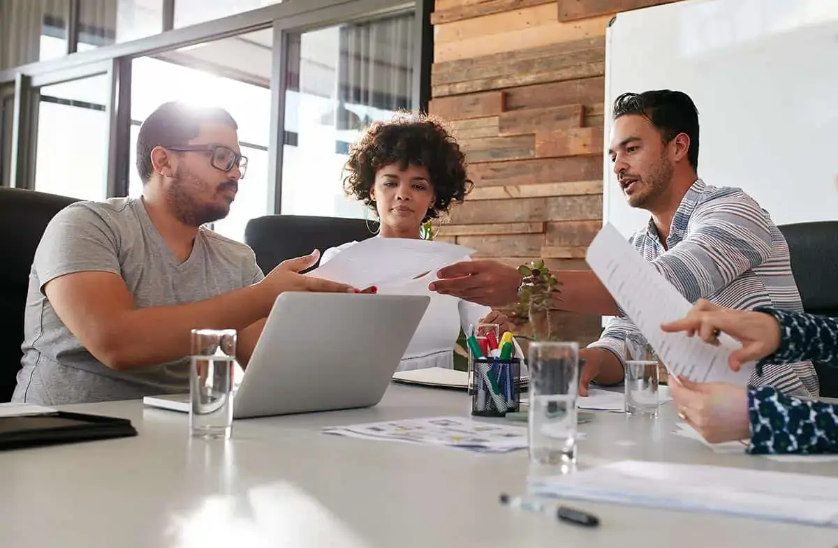 A group of people sitting around a table with a laptop. - UserVoice Images