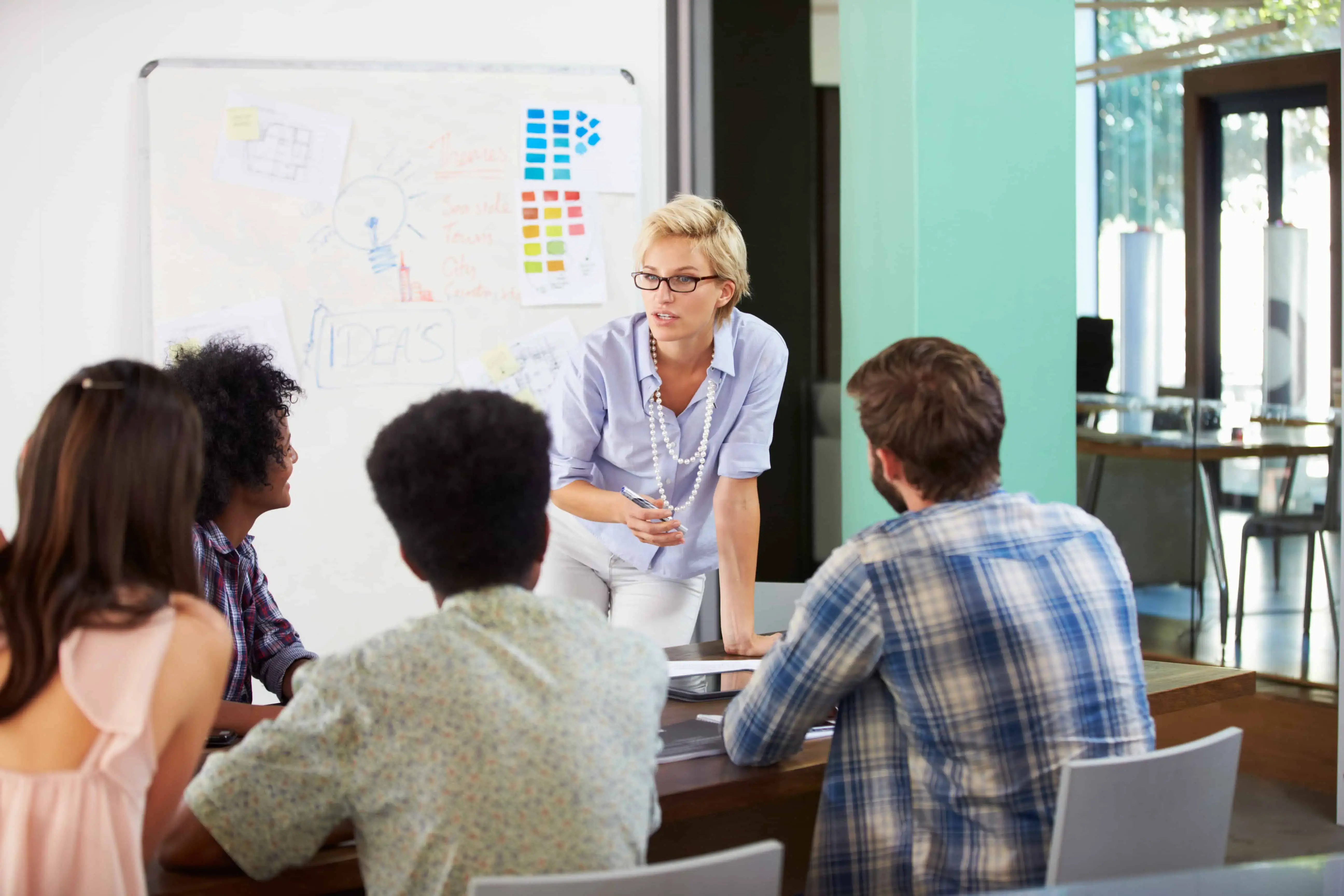A woman in a blue shirt and white pants stands in front of a white board. - UserVoice Images