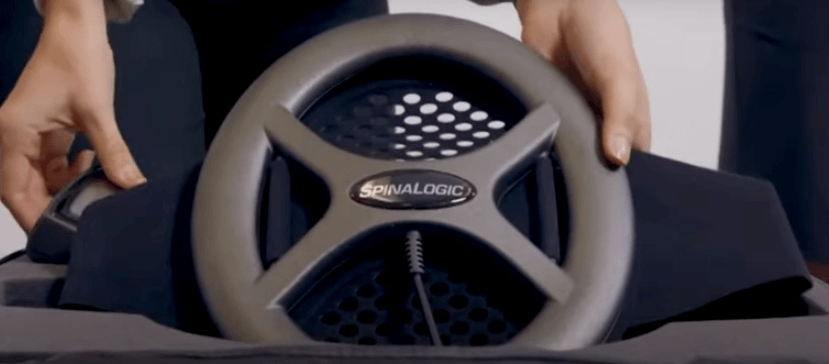 Hands adjusting a Spinalogic medical device wheel with a cable and perforated background.